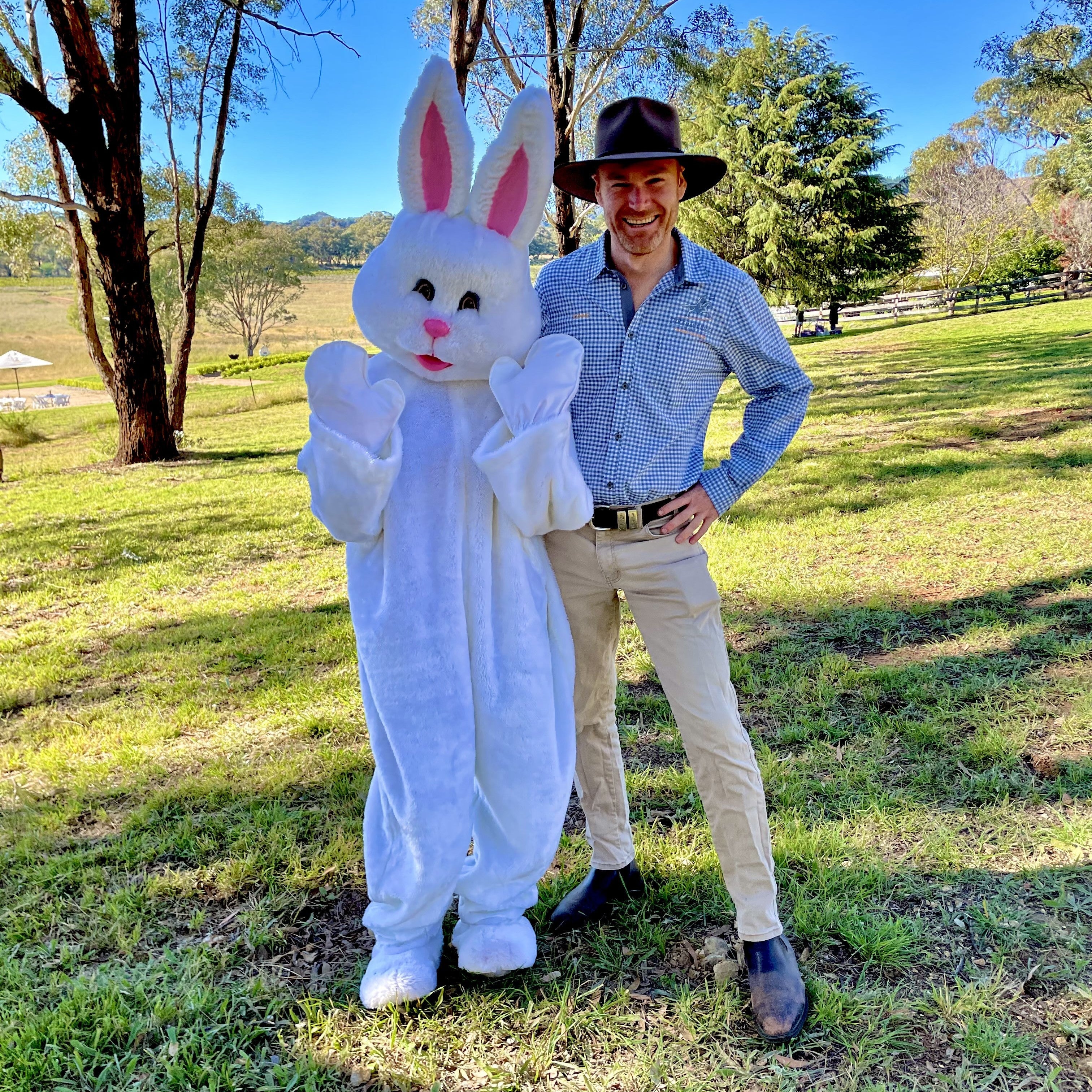 A person in an Easter bunny costume standing next to a man in a hat and shirt, outdoors at Stockman's Ridge Wines