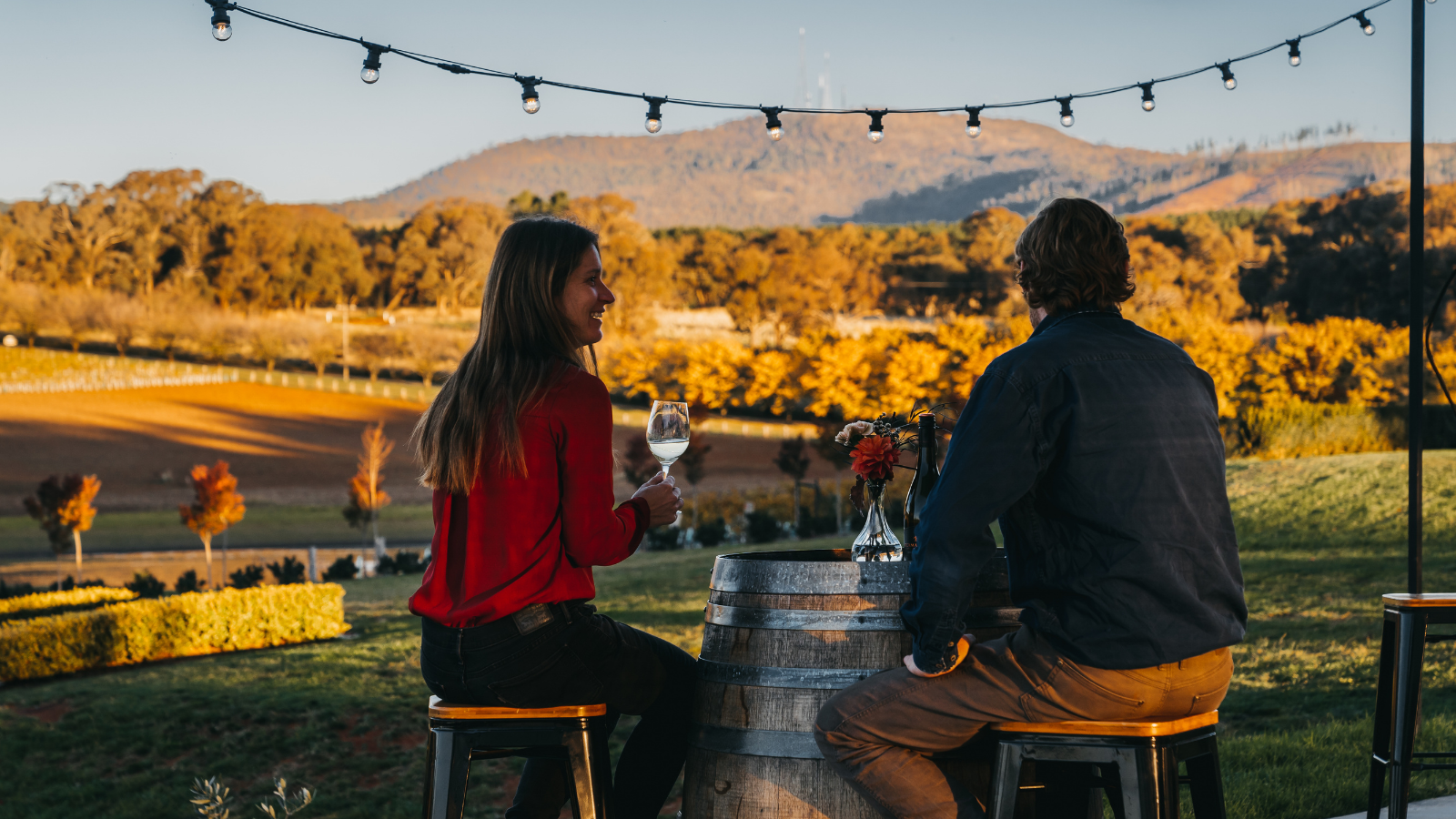 Two people sitting on barrels outdoors with a scenic background
