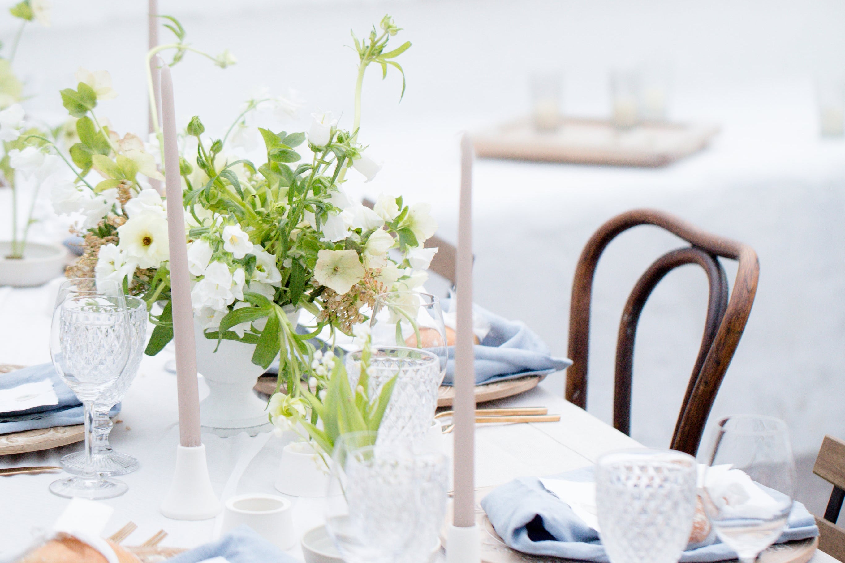 Elegant table setting with flowers, candles, and glasses on a white tablecloth.