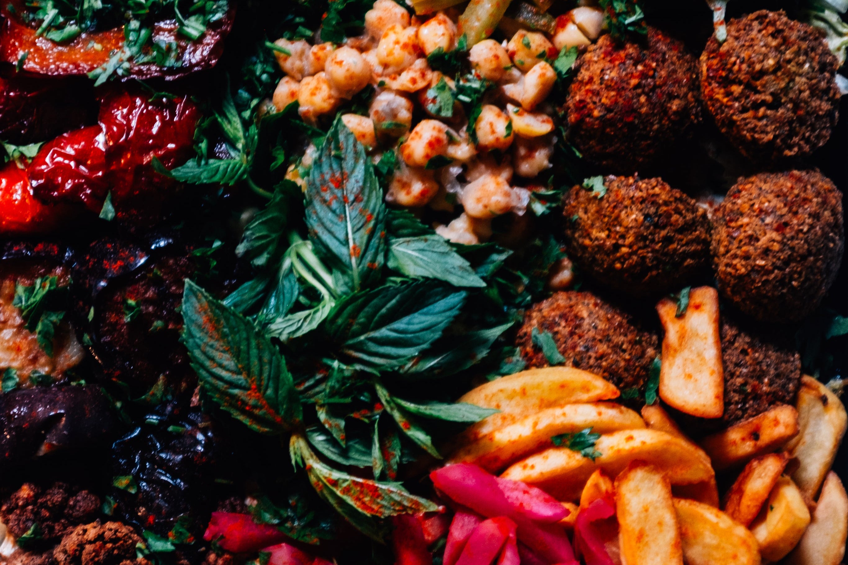 Assorted snacks including falafel, hummus, and vegetables on a dark background
